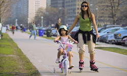 Mother skating with her young daughter riding a bike on the sidewalk